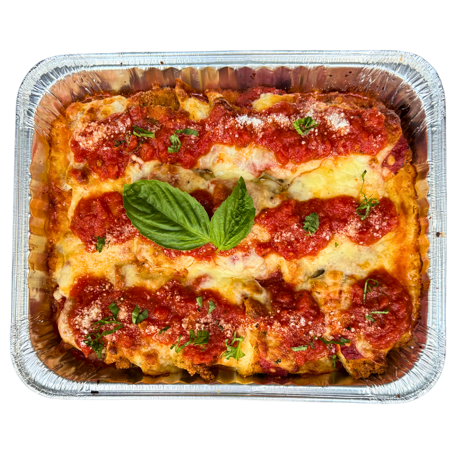Family size Chicken Parmigiana in a foil container, topped with cheese and tomato sauce, garnished with a basil leaf.