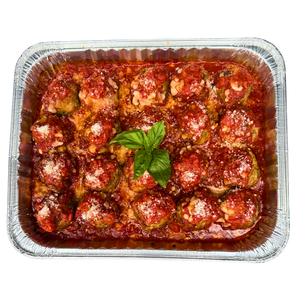 A family size tray filled with baked meatballs covered in tomato sauce and cheese, garnished with a basil leaf.
