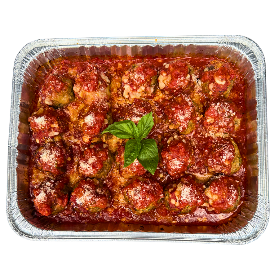 A family size tray filled with baked meatballs covered in tomato sauce and cheese, garnished with a basil leaf.